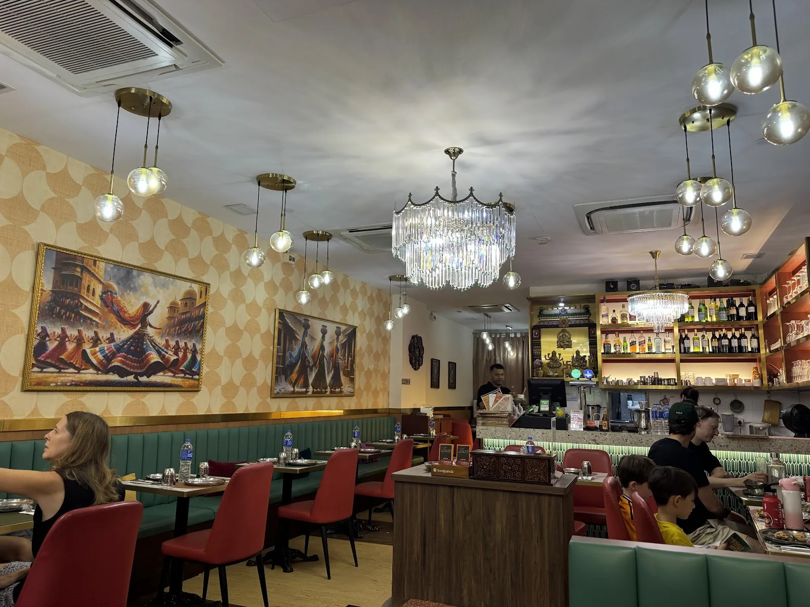 Inside Tulsi - green banquettes, red chairs and chandeliers around a backlit bar